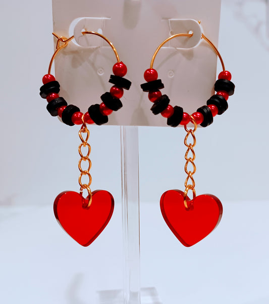 Small gold hoop earrings featuring black and red beads with a red acrylic heart charm