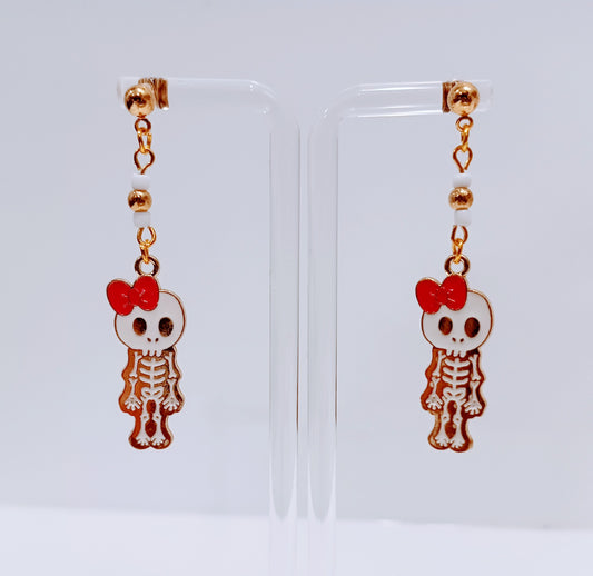 Gold enamel earring with a white skeleton wearing and pink bow. 
